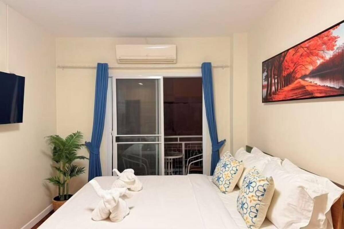 A hotel room with a bed, a potted plant, a painting, and a view of the outside.