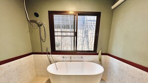 Une salle de bain avec une baignoire sur pieds, une fenêtre donnant sur une clôture et un porte-serviettes.