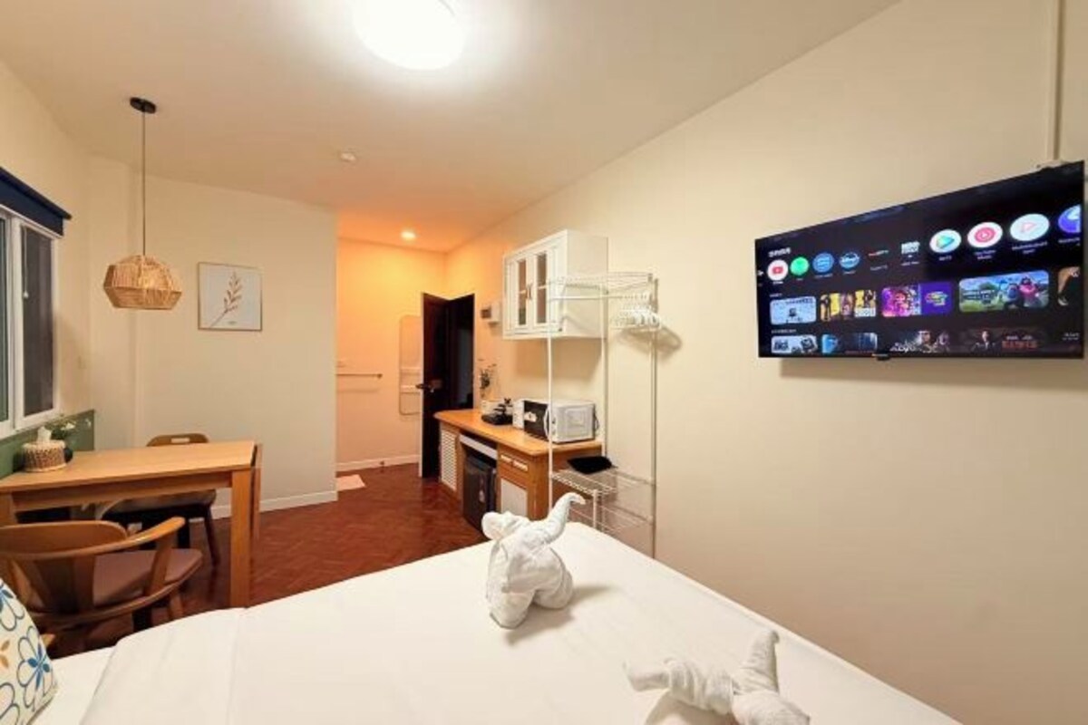 Une chambre d’hôtel comprenant un lit, un bureau avec des chaises, un téléviseur fixé au mur et un coin cuisine.
