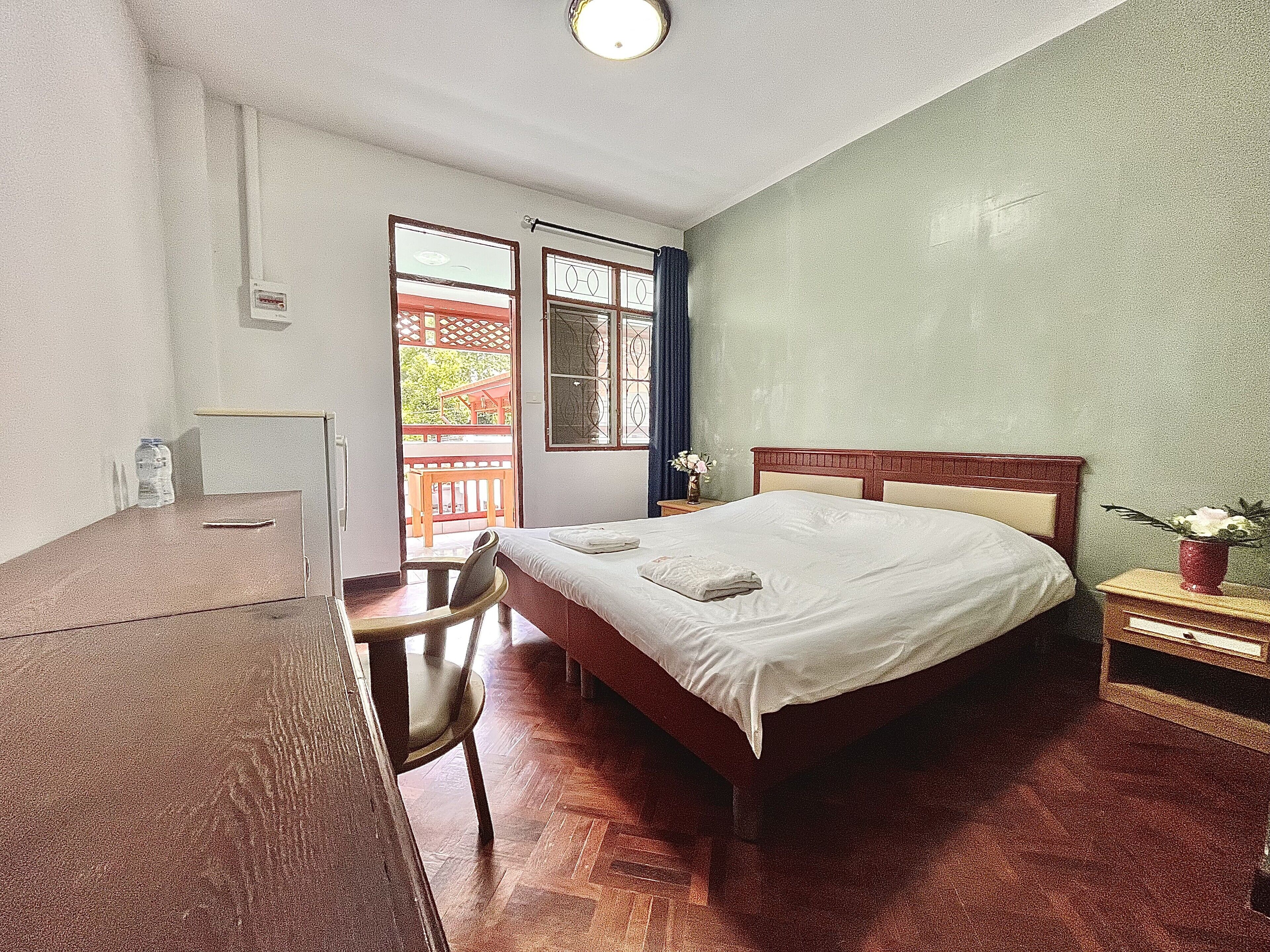 A bedroom with a bed, a desk, and a chair. There is a window with a view of a balcony.