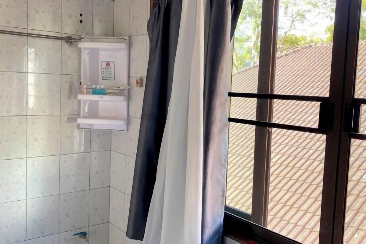 A bathroom with a white tiled wall, a white cabinet with a water dispenser, and a window with a view of a tiled roof outside.