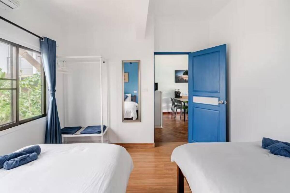 A hotel room with two beds, a desk, a chair, a mirror, and a blue door.