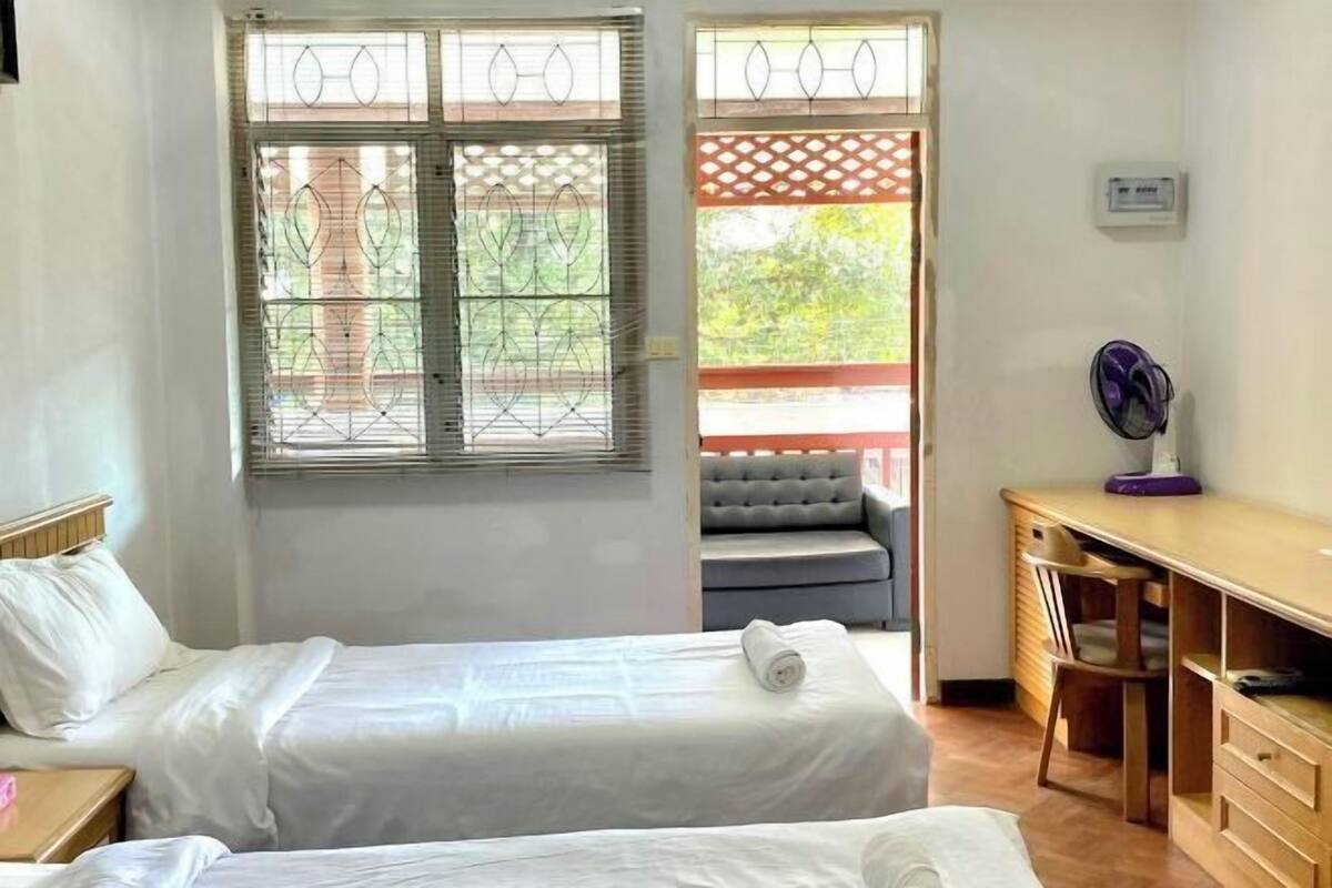 A bedroom with two beds, a desk, a chair, and a window with a view of greenery.