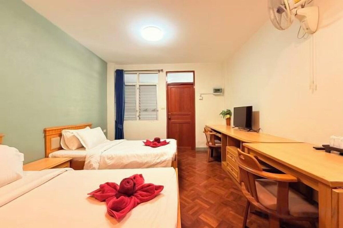 Une chambre d’hôtel avec deux lits, un bureau, une chaise, une télévision et une fenêtre avec des rideaux.