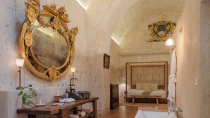 Ein Badezimmer mit einer Badewanne, einem großen, verzierten Spiegel, einem hölzernen Waschtisch und einem Bett mit Holz Kopfteil.
