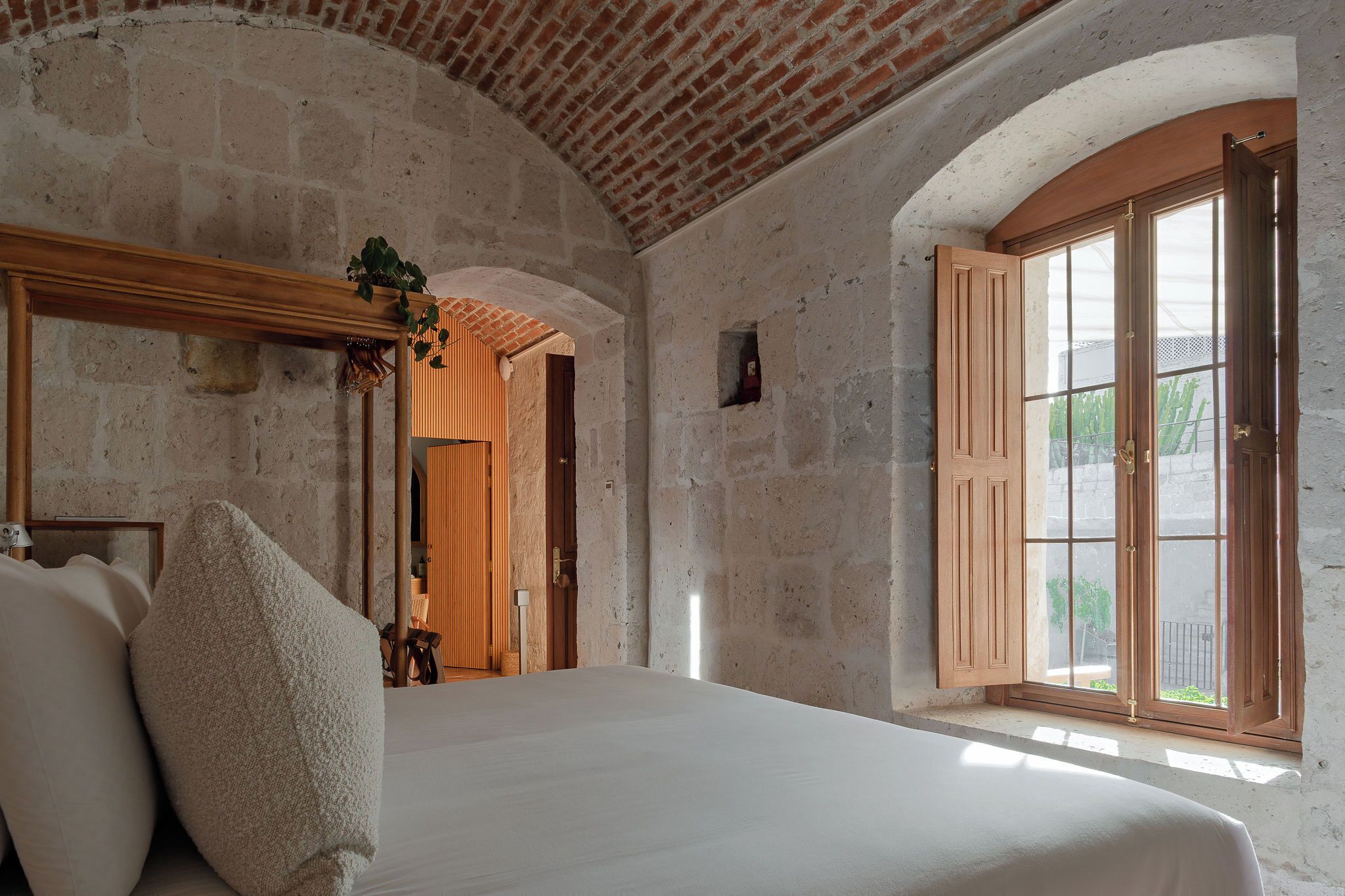 A room with a bed, a wooden door, a window, and a stone wall.