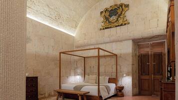 Una habitación con una cama con dosel, un banco de madera, un aparador y una puerta.