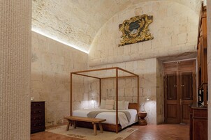 Una habitación con una cama con dosel, un banco de madera, un aparador y una puerta.