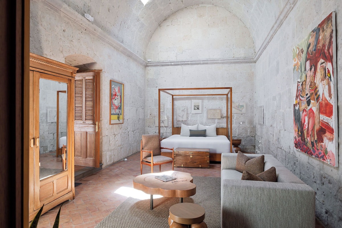 A bedroom with a four-poster bed, wooden furniture, and a large painting on the wall.