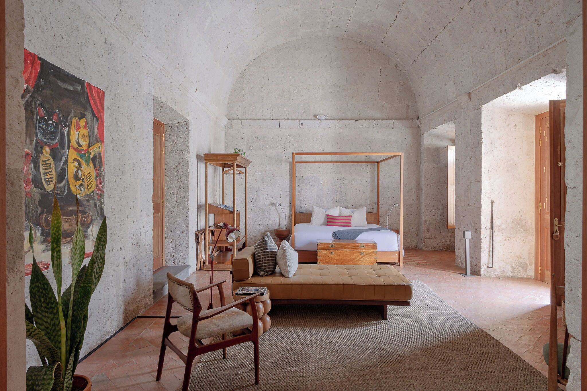 Een slaapkamer met een hemelbed, een houten stoel, een bureau en een groot schilderij aan de wand.
