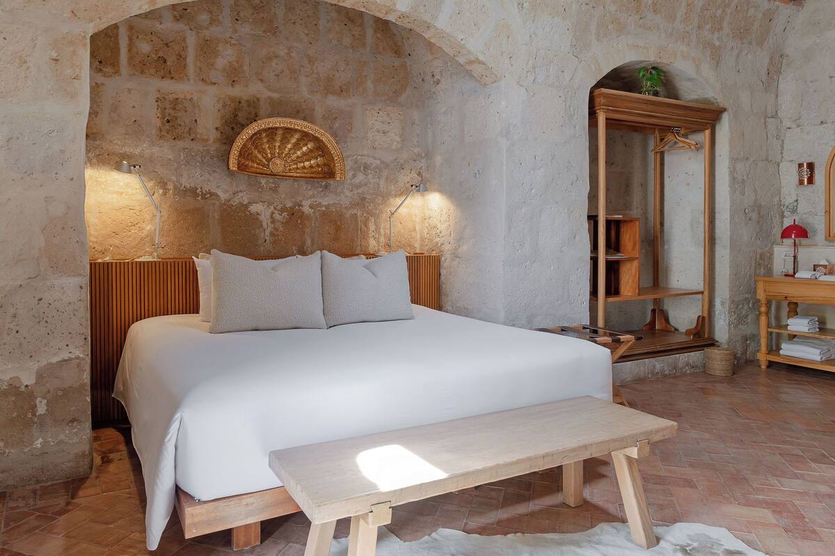 A bedroom with a bed, bedside table, lamp, and a mirror.