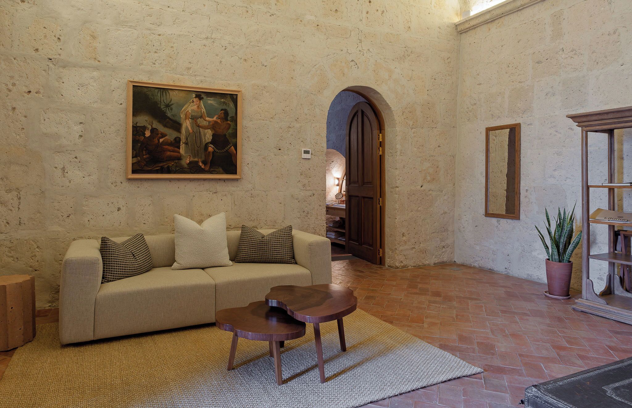 Una habitación con sofá, una mesita, un cuadro, un arco de entrada y una planta en maceta.