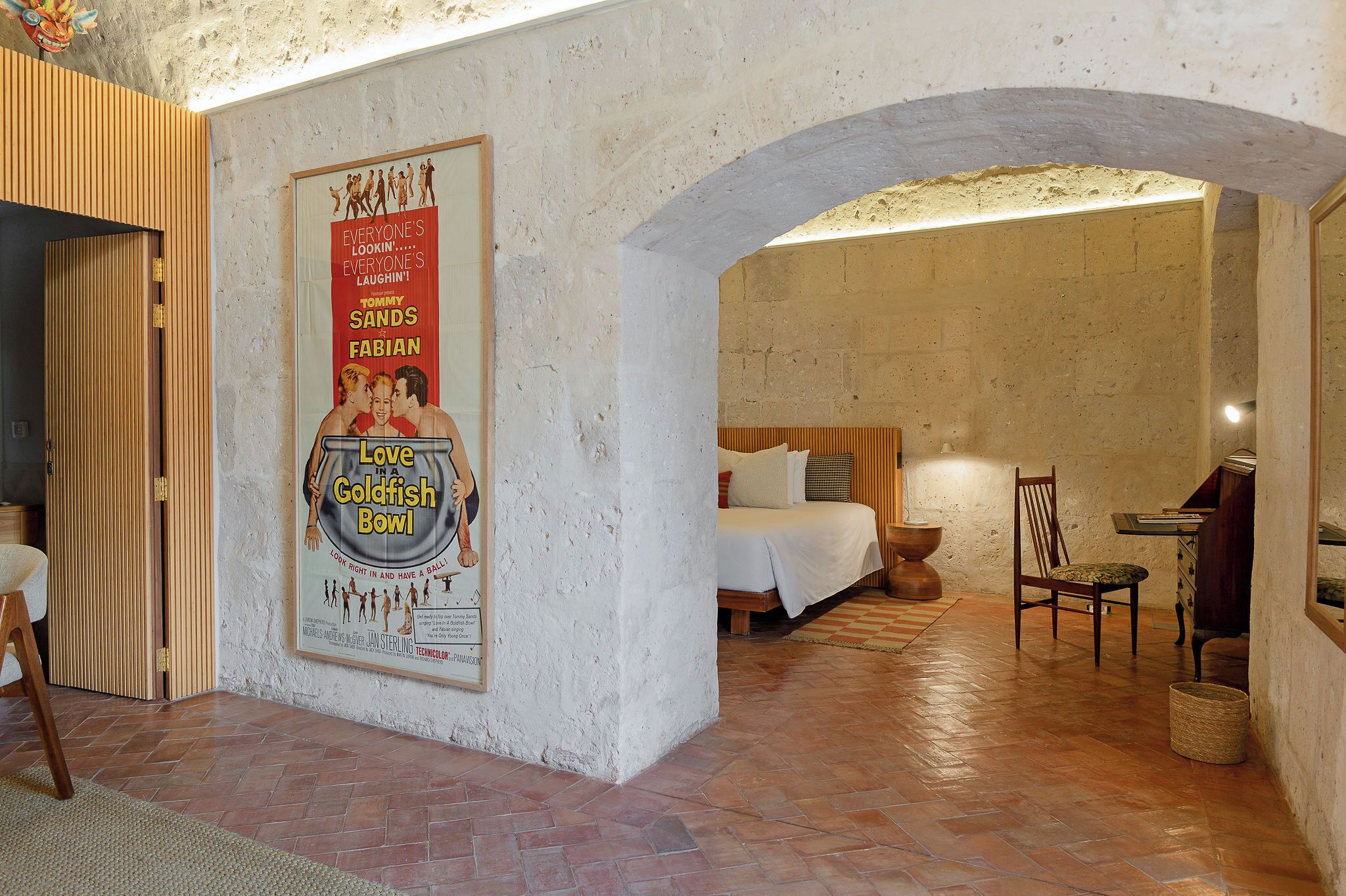 Una stanza con un letto, una sedia, un tavolo e un quadro appeso al muro.