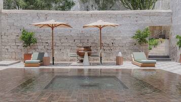 Zona de piscina con dos sillones, dos sombrillas, una mesa y una maceta decorativa.
