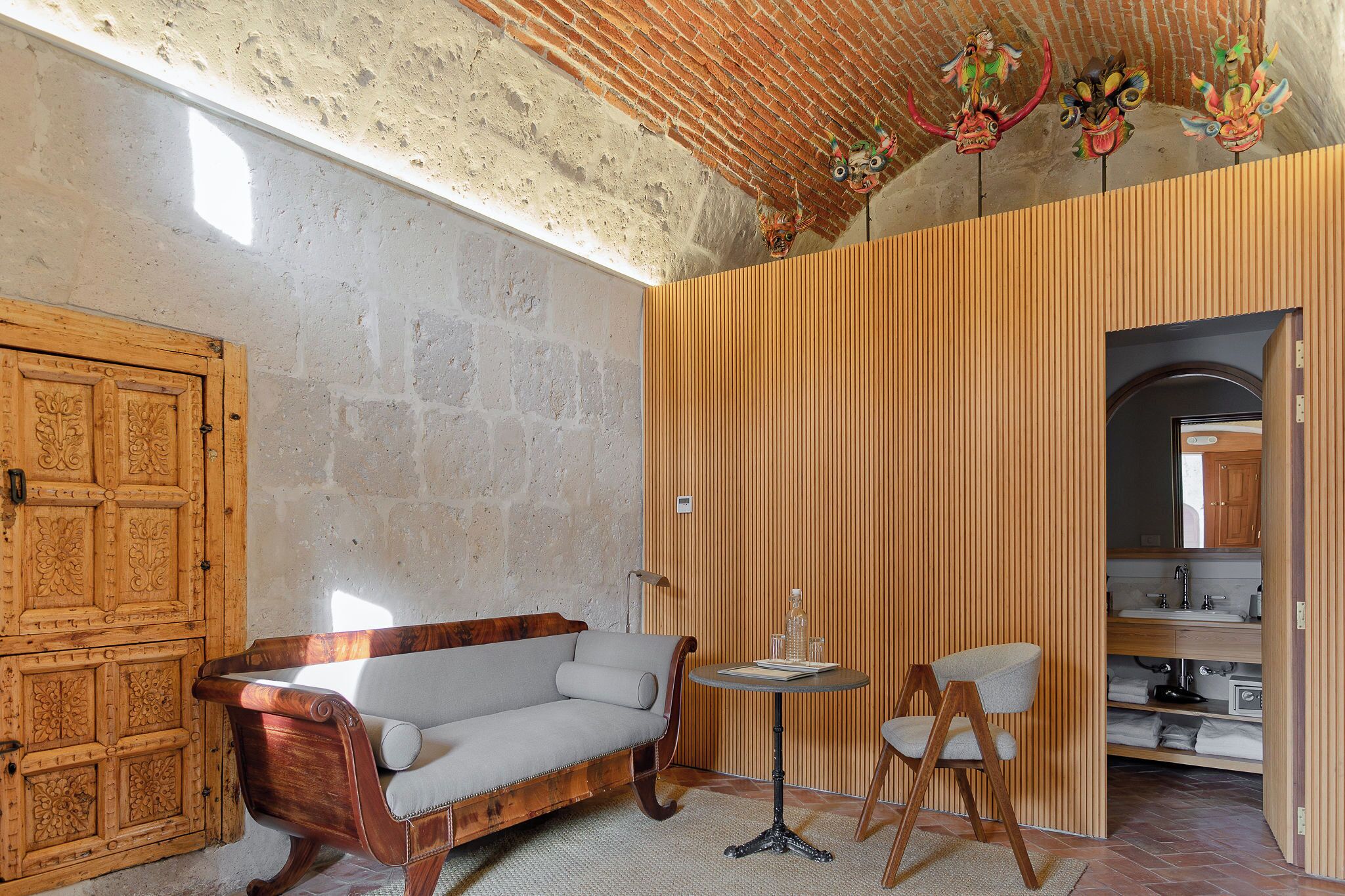 Une pièce avec une porte en bois, un banc rembourré, une petite table ronde et une chaise.