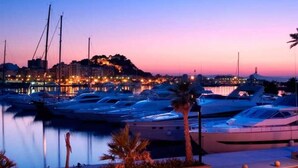 A marina at dusk with yachts docked, a cityscape in the background, and palm trees in the foreground. - Casa Solanilla Entre mer et Golf (La Sella)