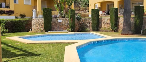 A hotel with two swimming pools, a stone wall, and a palm tree.