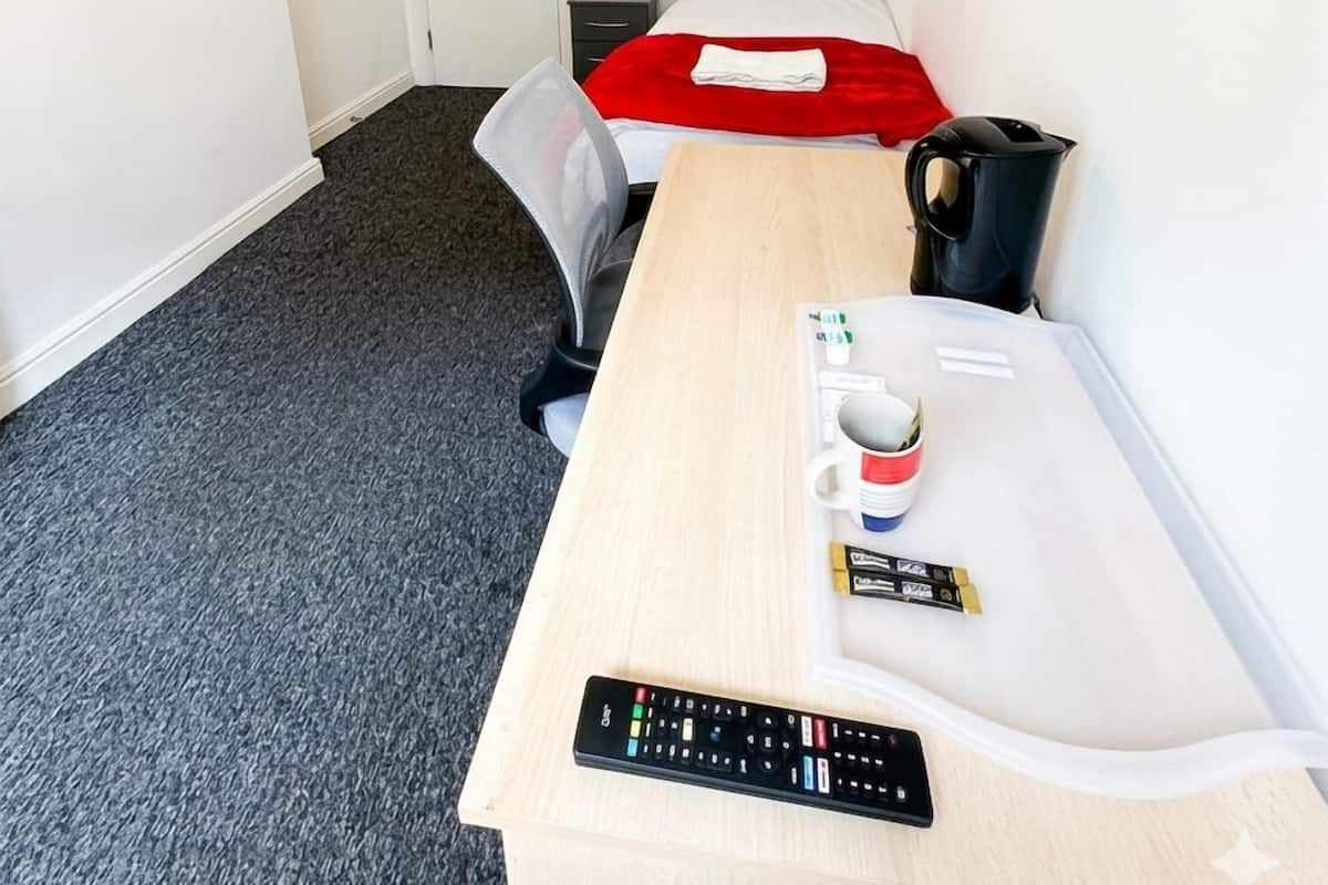 Una habitación de hotel con cama, escritorio con control remoto, cafetera y puerta.
