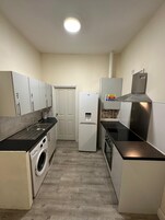 Una cucina compatta con lavatrice, frigorifero e piano cottura.
