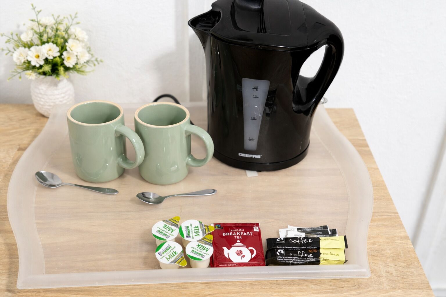 A tray with two green mugs, a black coffee maker, a spoon, and various tea and coffee packets.