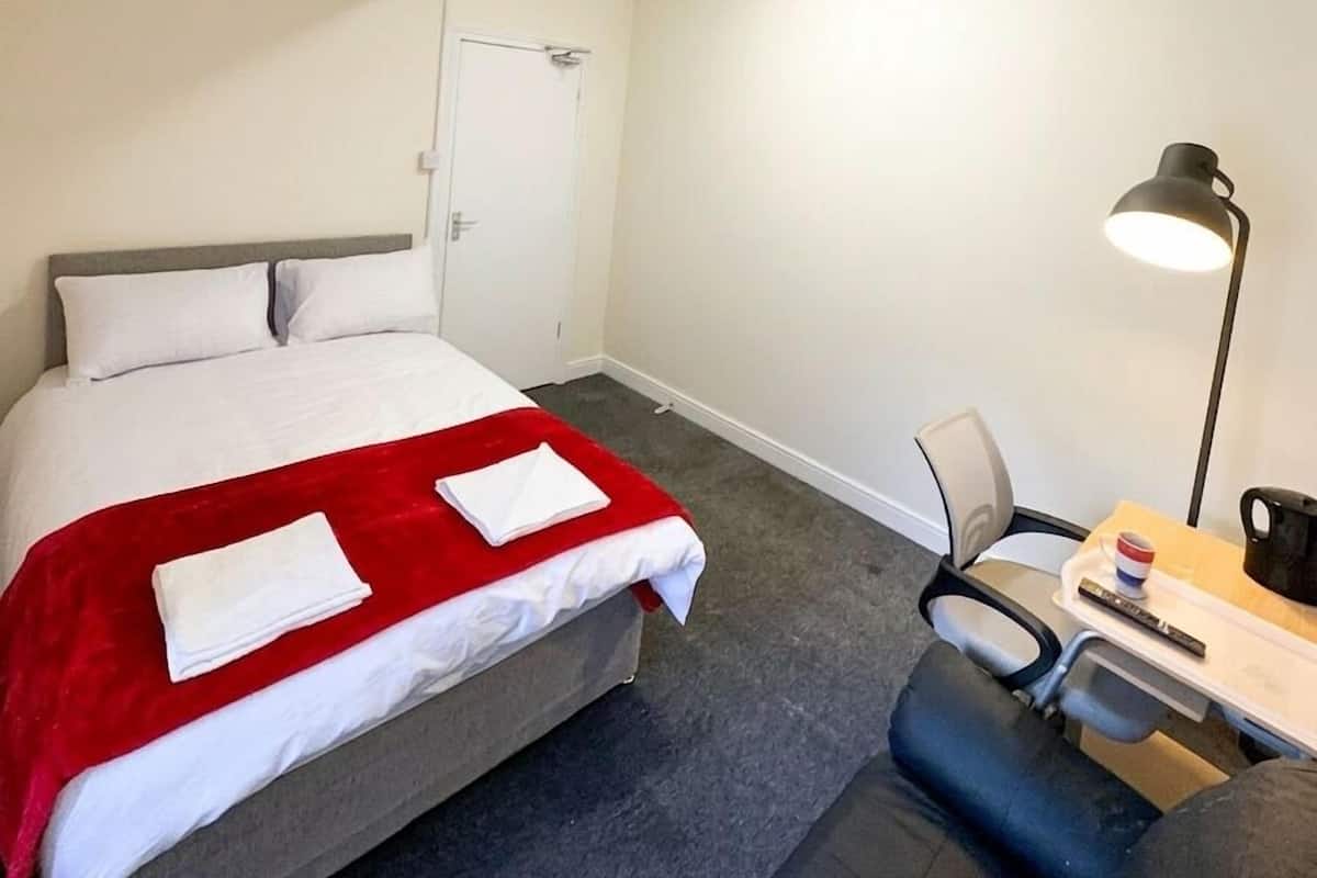 Una habitación de hotel con cama, escritorio, silla, lámpara y puerta.