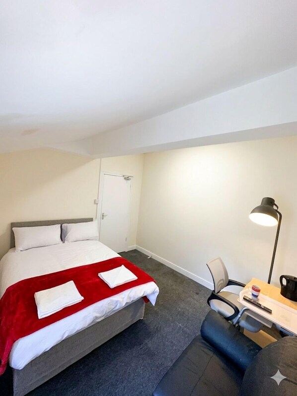 A hotel room with a bed, a desk, a chair, a lamp, and a door. - Macclesfield Lodge (Macclesfield)