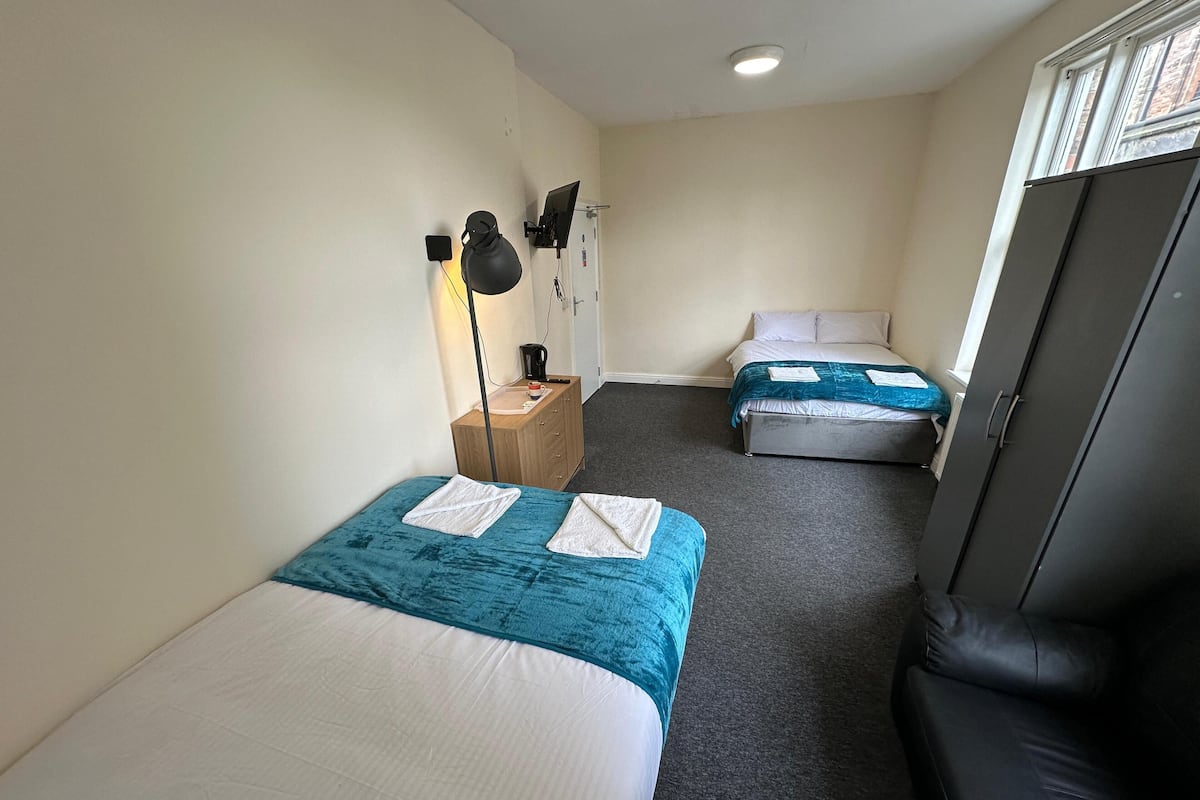 Habitación de hotel con dos camas, un escritorio con lámpara, un armario y un sofá.