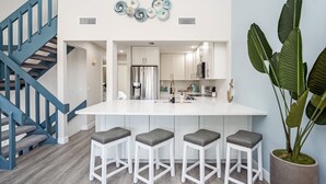 A modern kitchen with a central island, bar stools, and a staircase with blue railings. - Sandy Toes Siesta dream stay 
800' to private beach access. 3 Bed 3 Bath (Sarasota)