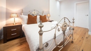 Une chambre à coucher avec un lit blanc, des oreillers marron, une table de chevet en bois et une lampe de chevet.