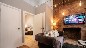 Un salon chaleureux avec une cheminée, un téléviseur fixé au mur diffusant une chaîne de divertissement, et un coin salon confortable.
