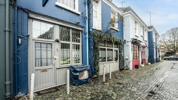 Une rangée de maisons mitoyennes aux façades bleues et blanches, une rue pavée et une voiture garée.