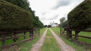 A gravel path leading to a white house with a traditional design, surrounded by well-maintained hedges and a wooden fence.