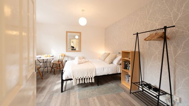 A bedroom with a bed, bedside table, chair, and a hanging rack.