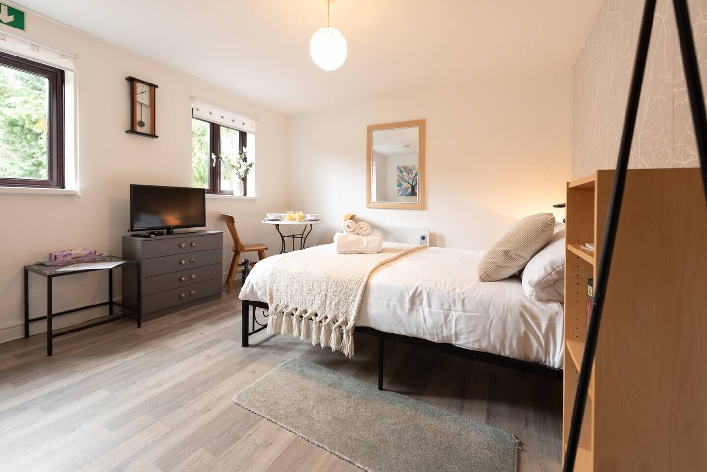 A bedroom with a bed, a desk, a dresser, a chair, a small table with a vase, and a window with curtains.