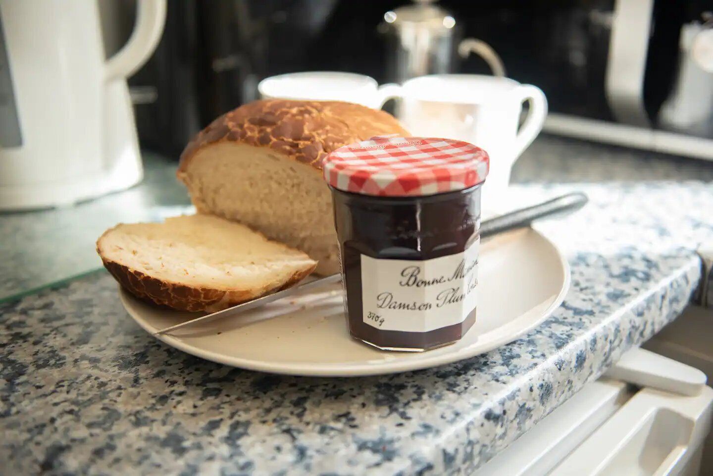 A plate with a loaf of bread and a jar of jam on a kitchen counter.