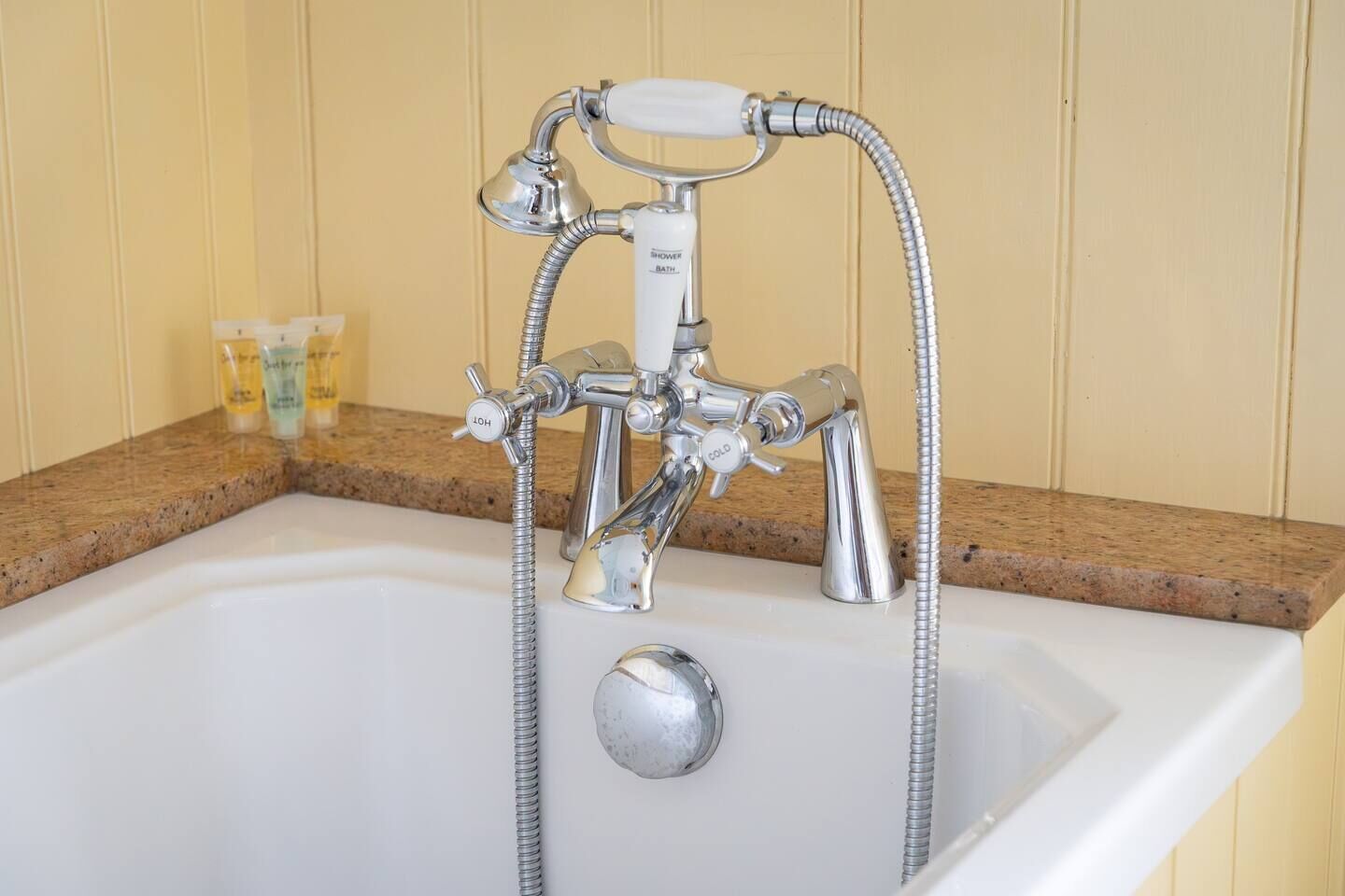 Une salle de bain avec une baignoire chromée, un pommeau de douche à main et deux bouteilles de shampoing posées sur le comptoir.