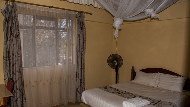 Een slaapkamer met een bed, gordijnen, een nachtkastje en een ventilator.