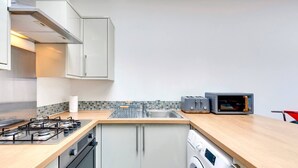 Ett modernt kök med en gasspis, en inbyggd ugn, en tvättmaskin, en mikrovågsugn och en brödrost.