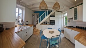 Eine moderne Küche mit weißen Schränken, einer Holzauskładung, einem blauen Essbereich und einer Treppe, die zu einer Loggia führt.