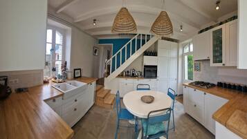 A modern kitchen with white cabinets, a wooden countertop, a blue dining area, and a staircase leading to a loft.