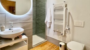 A bathroom with a round mirror, a sink, a toilet, a shower, and a towel rack. - Apartamento con Baño Adaptado (Astorga)
