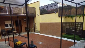 A covered patio area with a brick floor, outdoor furniture, and a view of the surrounding building. - Apartamento con Baño Adaptado (Astorga)