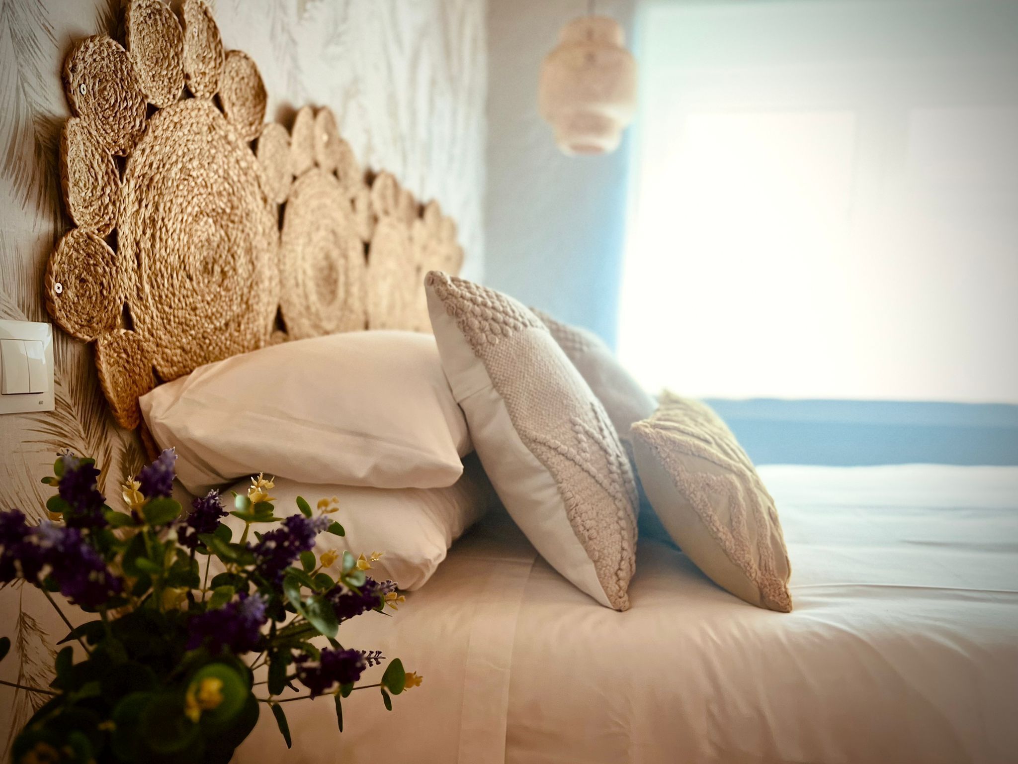 A bed with white bedding, a woven headboard, and two white pillows.