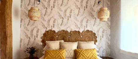 A bedroom with a bed, a wooden headboard, a wall with a leaf pattern, and two hanging lamps.