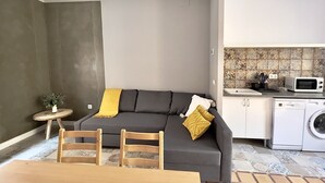 Um espaço habitável compacto com sofá, uma pequena mesa redonda, máquina de lavar e micro-ondas na área da cozinha.