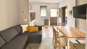 Um espaço compacto com sofá, mesa de jantar de madeira com cadeiras, cozinha equipada e televisão na parede.