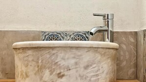 Ein rundes, weißes Keramikwaschbecken mit einem einzelnen Wasserhahn, eingebaut in eine Ecke mit dekorativer Fliesenfassade.