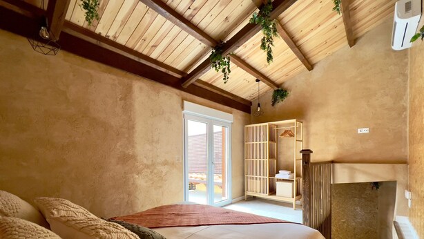 Ein Schlafzimmer mit einem großen Bett, Holzbalkendecke, einem Kleiderschrank und Blick durch eine Glastür.