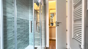 A modern bathroom with a glass shower enclosure, a white door with a radiator, and a wooden floor. - Espacioso Apartamento con Bañera (Astorga)