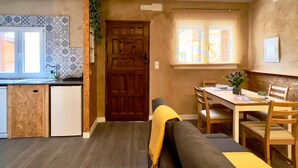 A compact kitchen with a wooden door, a dining area with a table and chairs, and a sofa with a yellow throw. - Espacioso Apartamento con Bañera (Astorga)